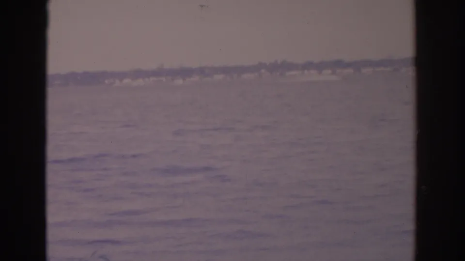 Faded 8mm frame from 1962 Florida showing rippled water, hazy shore, and dark vertical edge framing from a moving vessel.