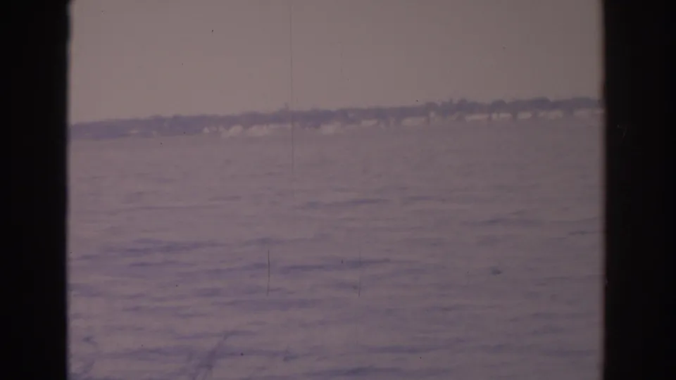 1962 Florida home-movie still showing calm water and a hazy shoreline through dark vessel or window framing.