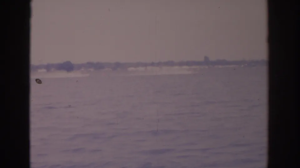 Window-framed 1962 Florida lake view with rippled water, muted sky, and faint buildings along the far shore.