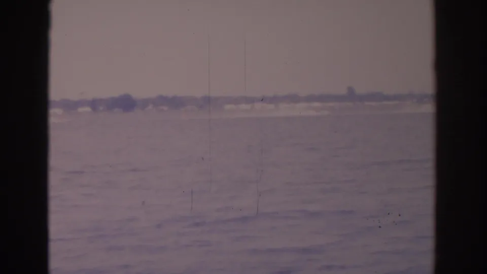 Soft 8mm view of a Florida lake in 1962, with far shoreline structures and dark window borders visible.