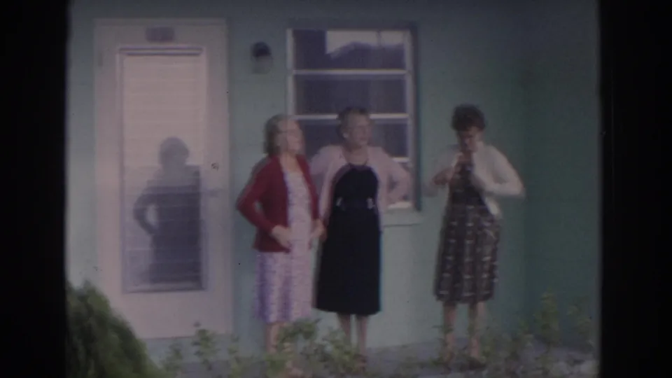 Three adult women in 1960s attire stand on a porch outside a light green Florida house, with a screened door and window behind them.