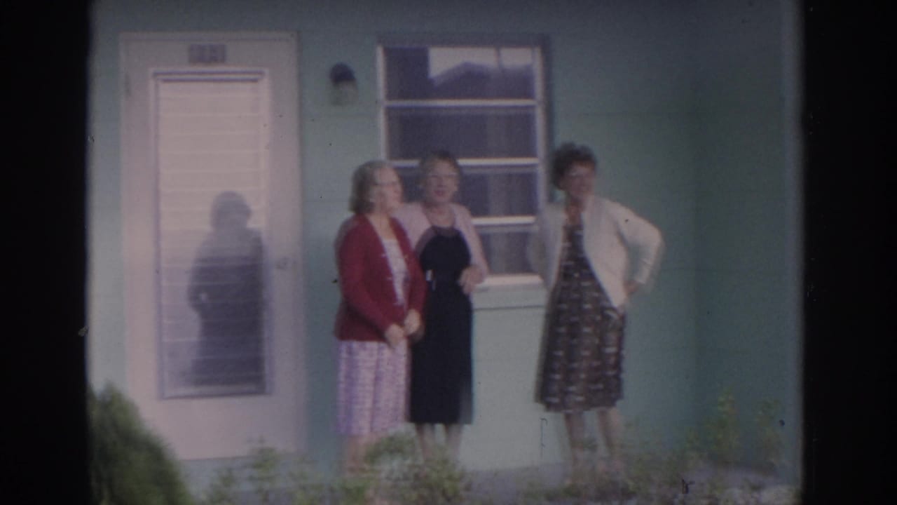 Three adult women pose outside a house, with a screened door and window behind them.