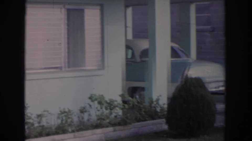 The camera drifts across the Florida house exterior, showing windows, porch columns, shrubs, and a partial vintage car in the background.