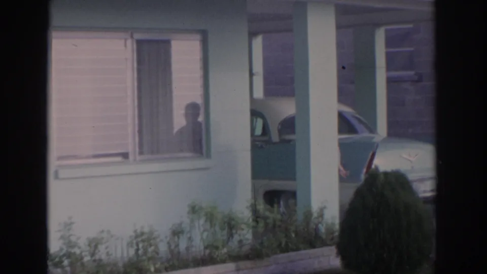 1962 Florida residential exterior with porch posts, window blinds, shrubs, and part of a late-1950s car in the driveway.