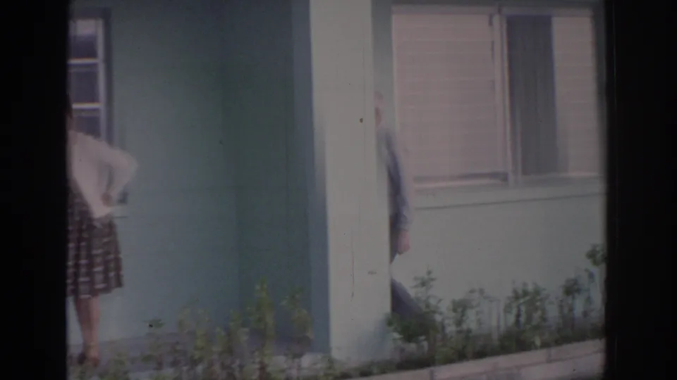 1962 Florida home exterior showing a woman near the entry and an elderly man partly leaving the frame beside the window.
