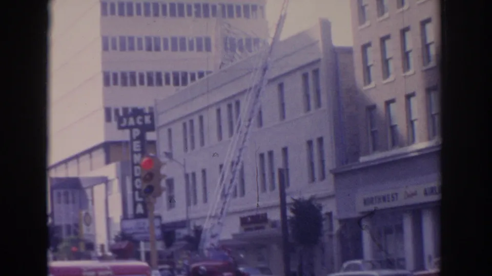 1962 Florida frame showing an extended fire ladder rising over a commercial street with building facades and signs.