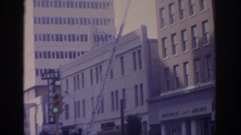 1962 Florida 8mm frame with an extended fire ladder, traffic signal, mid-century storefronts, and upper building windows.