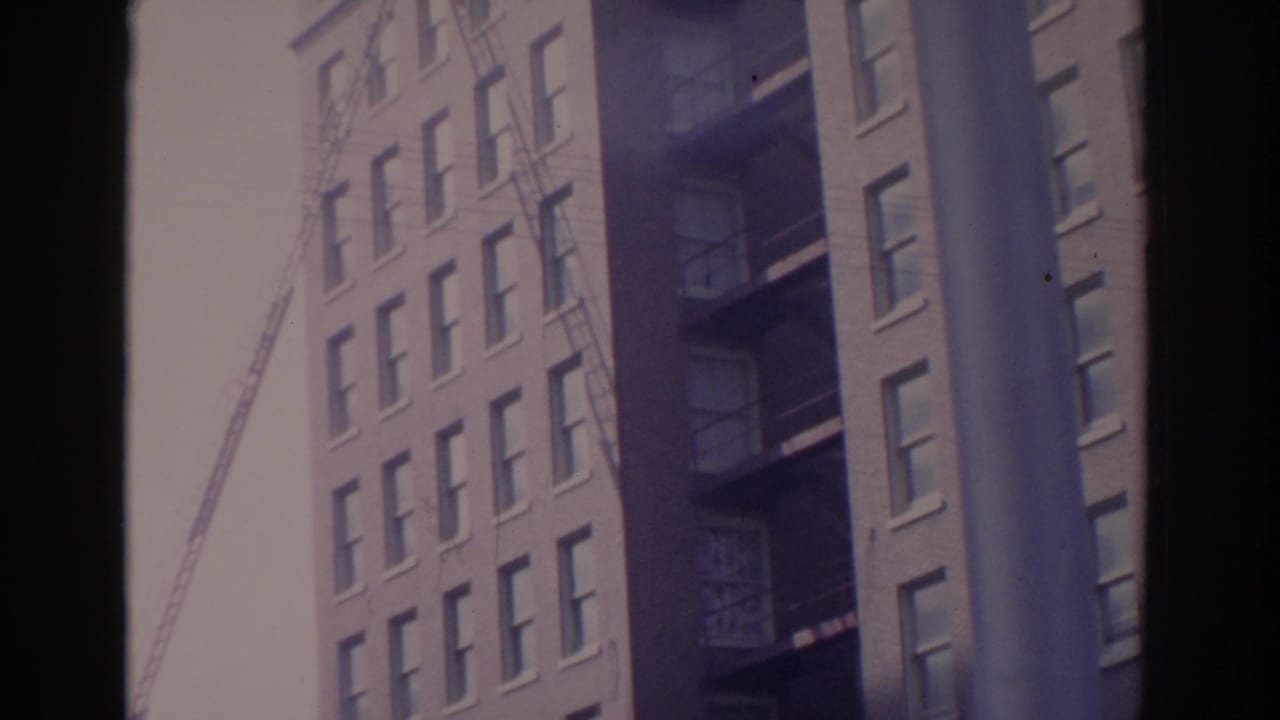 Tall brick buildings, fire escapes, and a crane framed by dark vertical borders.