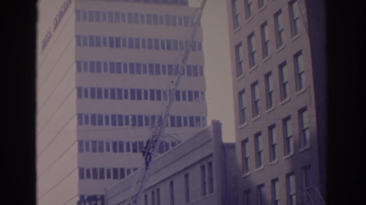 Pale office tower, crane boom, and adjacent brick building seen through dark borders.