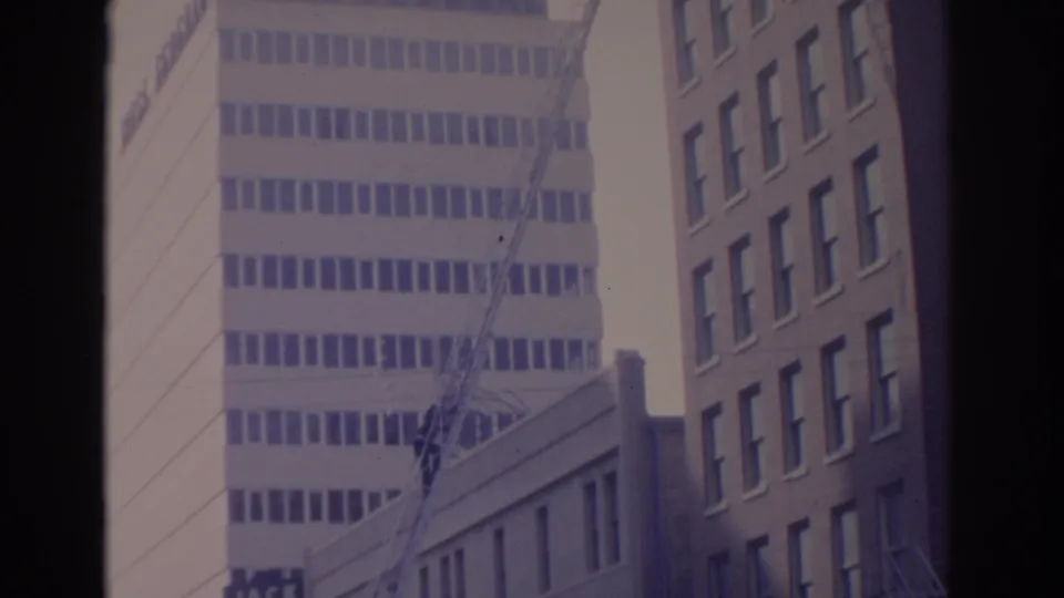 1962 Florida frame with a modern pale office tower, crane boom, low roofline, and brick building edge in a soft 8mm scan.