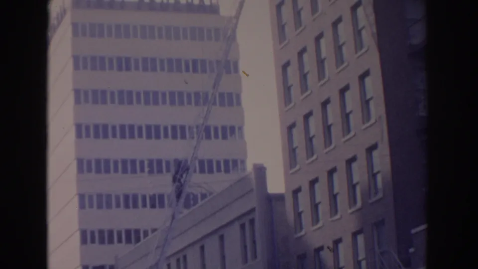 1962 Florida 8mm frame showing tall urban buildings, a lower facade, and possible overhead wires viewed from street level.