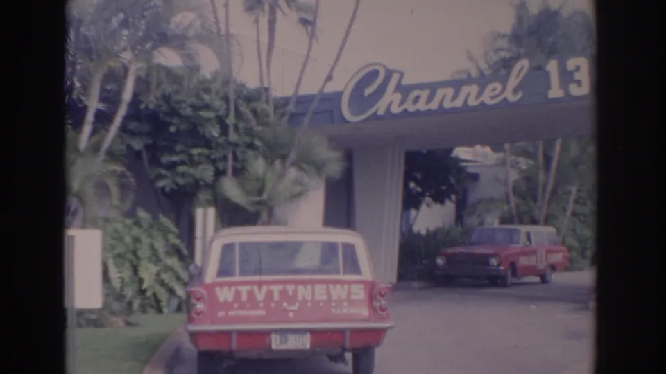 1962 Florida frame of the Channel 13 building entrance with a WTVT NEWS wagon in front and another red vehicle under the canopy.