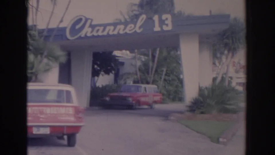 1962 Florida frame showing the Channel 13 canopy, tropical landscaping, a partly cropped WTVT NEWS wagon, and a red car beyond it.