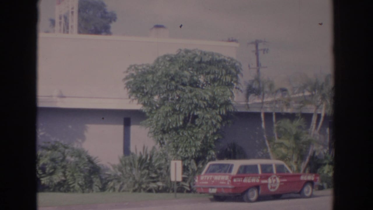 Red Channel 13 news station wagon parked outside a palm-lined building.