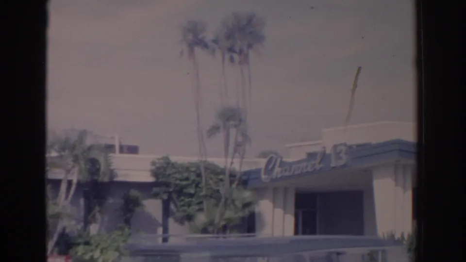 Florida station exterior with Channel 13 signage, palm trees, and the top of a vehicle crossing the lower frame.