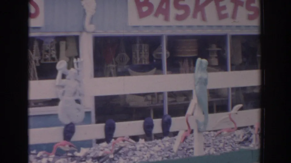 Final frame of the Florida souvenir shop showing the baskets sign, white railing, blue posts, mermaid figure, and window merchandise.