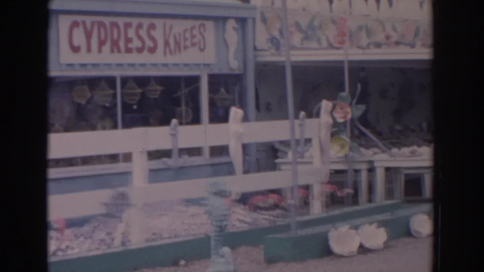 1962 Florida home-movie frame of the Cypress Knees shopfront with shells, fencing, and painted marine decorations.