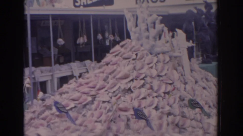 1962 Florida home-movie frame of a shell mound and marine decorations outside a storefront with partial Shells and Bags signs.