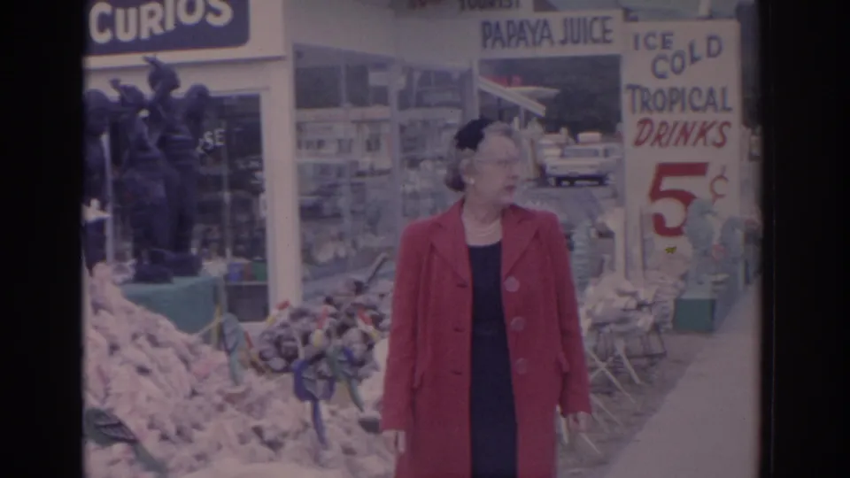 A Florida market frame shows the woman near shell souvenirs, storefront windows, and hand-painted signs for papaya juice and tropical drinks.