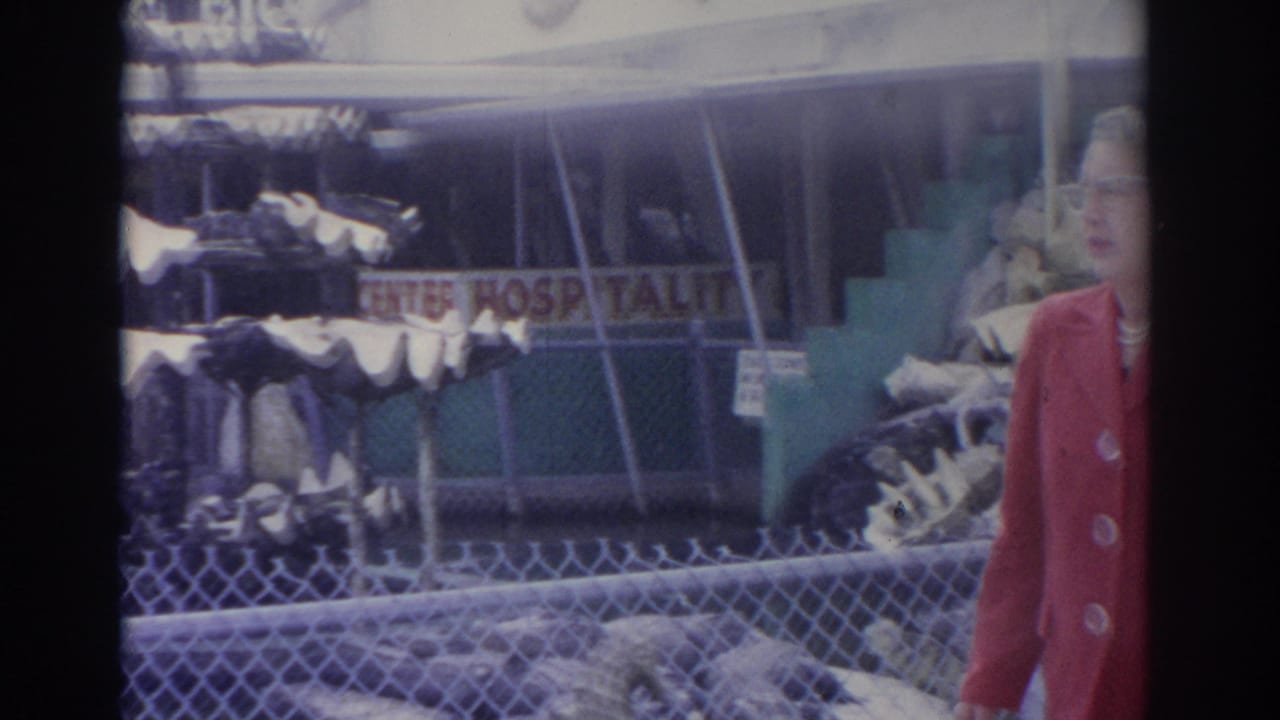 Woman in red at the right edge of a fenced zoo display with bones and a sign in the background.