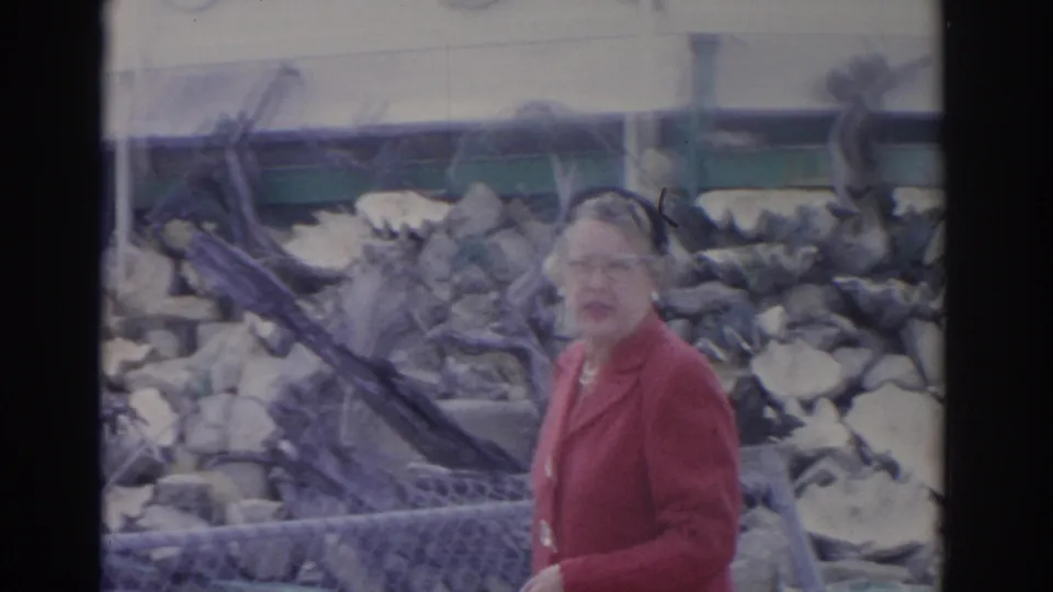 The woman in red faces toward the camera while standing near the fenced animal bone display in the Florida 1962 zoo scene.