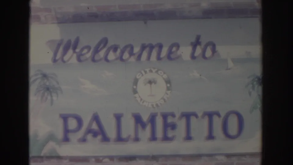The Palmetto welcome sign fills the lower frame, showing painted lettering, palm imagery, and soft 8mm color fading.