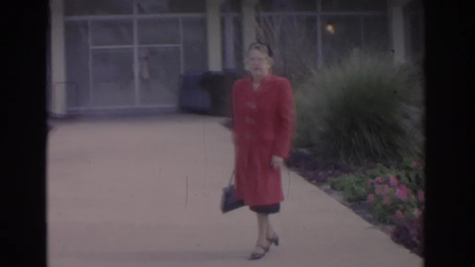 The woman in a red coat and hat walks through a landscaped Florida garden in this 1962 home-movie frame.