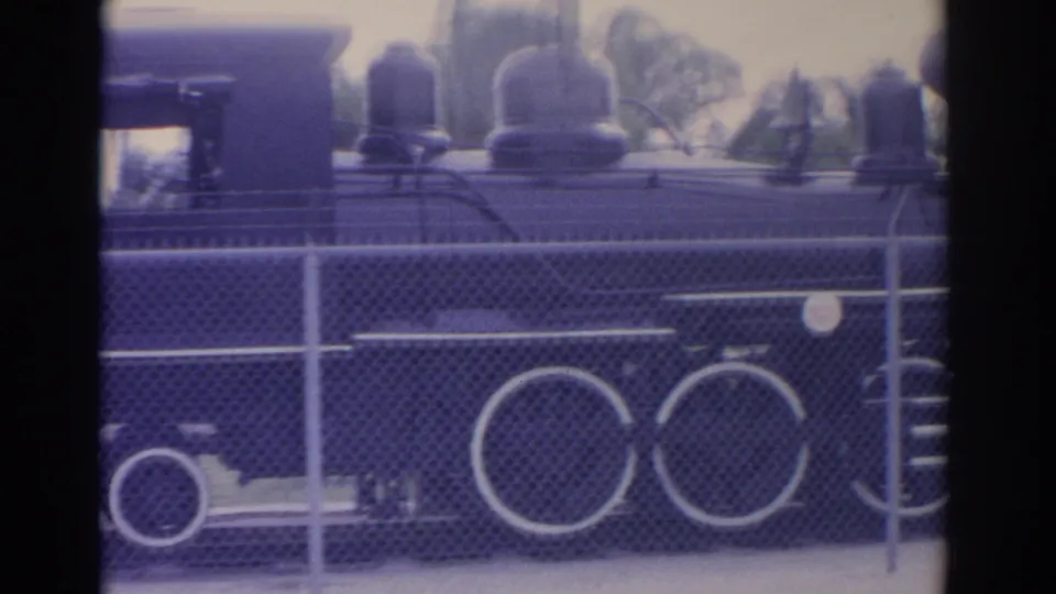 Final 1962 Florida frame showing the side of a black steam train replica, large wheels, and fence foreground.