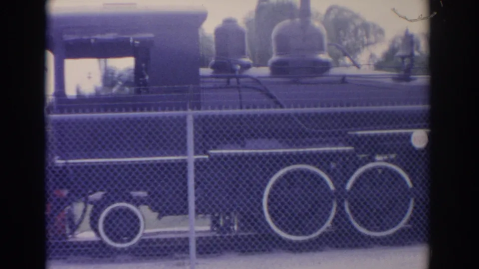 1962 Florida 8mm frame showing a dark steam locomotive behind chain-link fencing, with white-rimmed wheels and palm trees in the background.