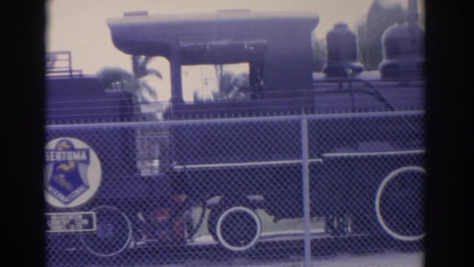 1962 Florida 8mm frame of a black steam locomotive behind fencing, with a Sertoma International emblem visible near the center-left.
