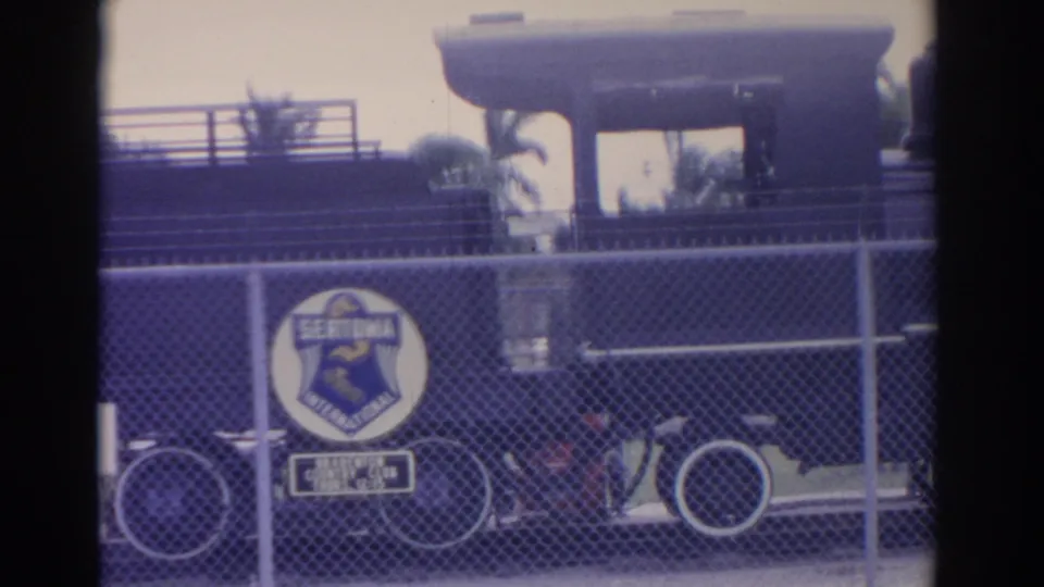 1962 Florida 8mm frame showing the Sertoma International emblem on fencing in front of a dark locomotive and white-rimmed wheel.