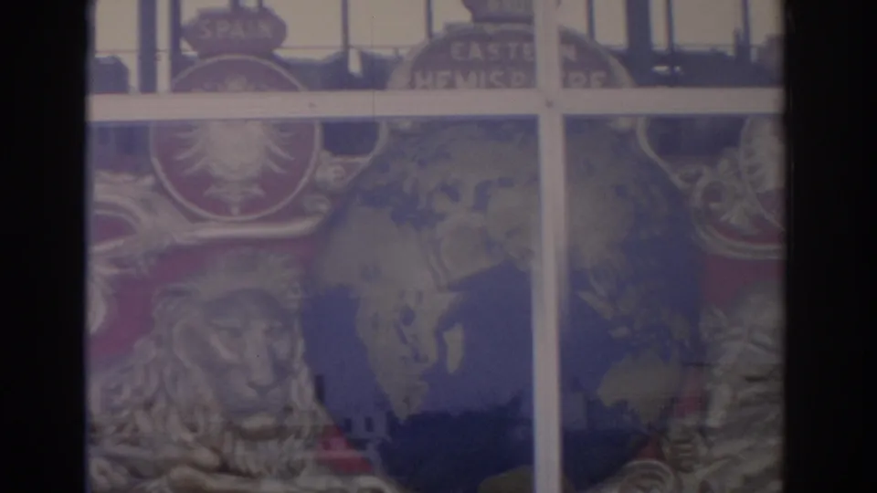 1962 Florida home-movie frame showing a lion figure, globe-like motif, and partial country labels through the attraction window.