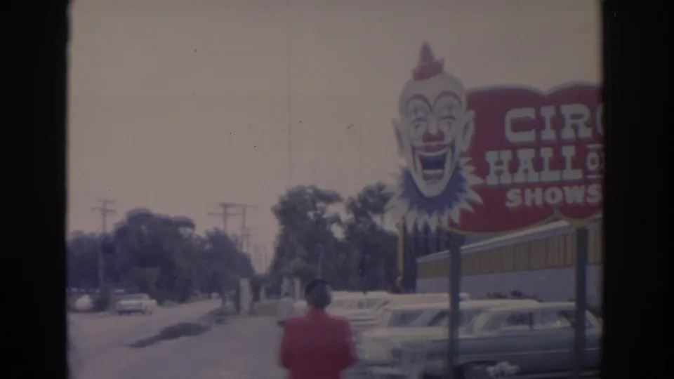 The billboard text reads Circus Hall of Fame Shows Daily as a woman walks past parked mid-century cars on a Florida roadside.