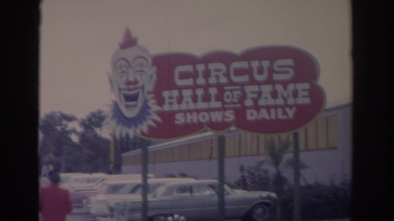 1962 Florida roadside view of a red and white Circus Hall of Fame sign with a clown face and early-1960s cars nearby.