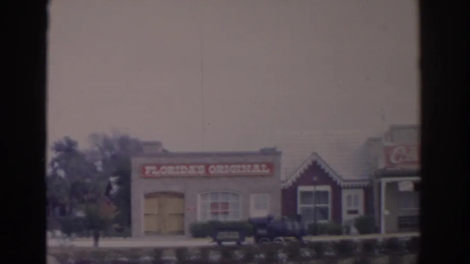 1962 Florida home-movie frame showing the Florida's Original building, hedges, and a small train display near the entrance area.