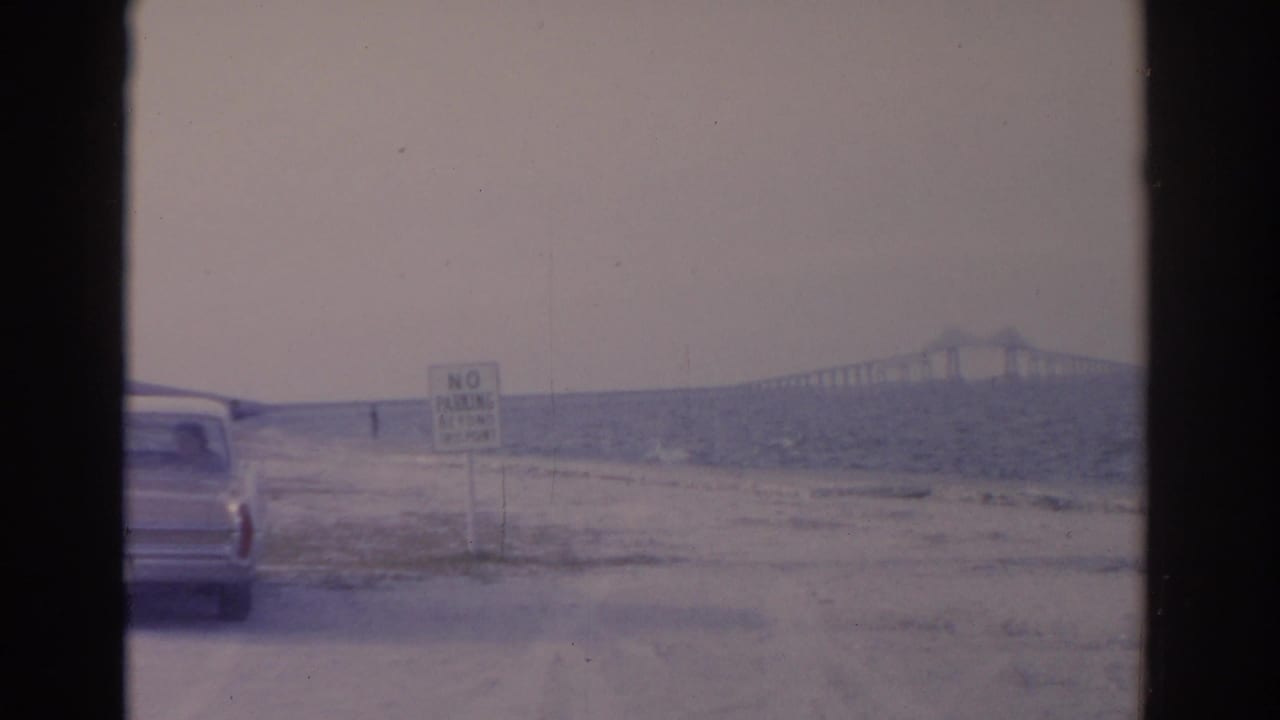 1962 Florida 8mm frame showing a roadside car, No Parking sign, choppy water, and a long bridge in the distance.