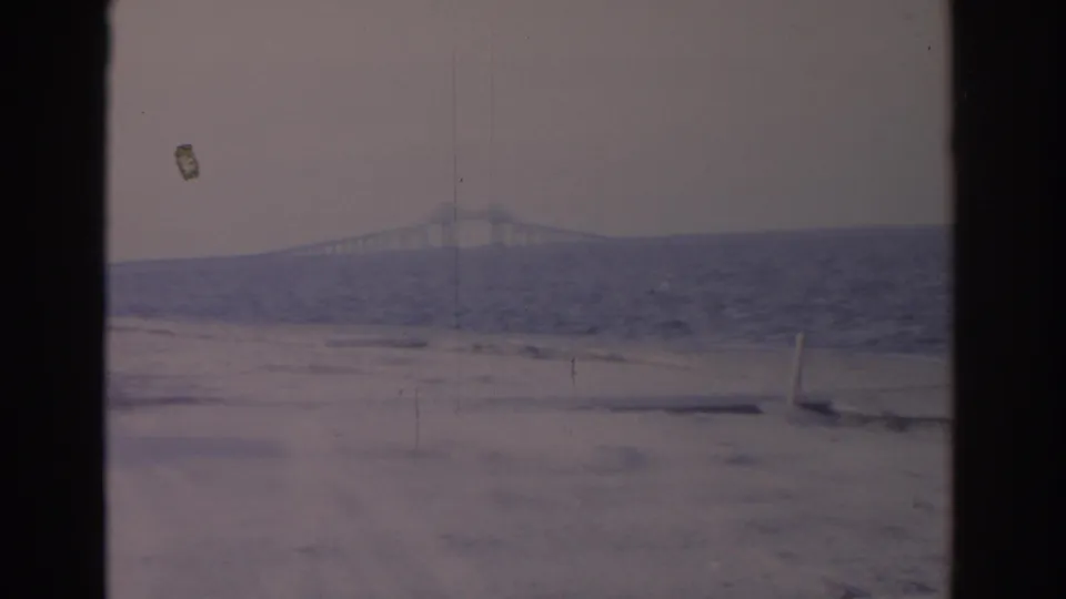 Faded 1962 Florida 8mm frame looking across a sandy coastal edge toward rough water and a long bridge in the distance.