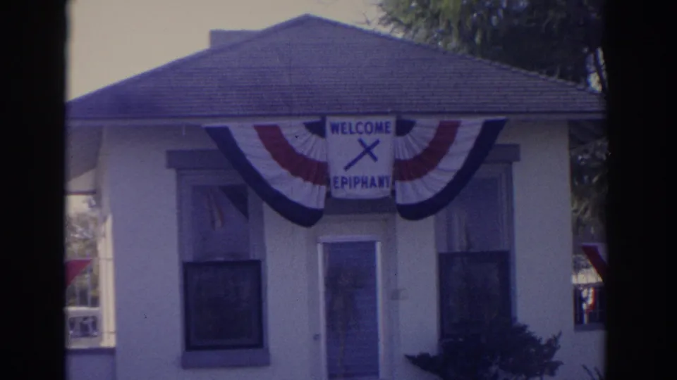 Florida 1962 frame of a small building decorated with patriotic bunting and a WELCOME EPIPHANY sign with a cross.