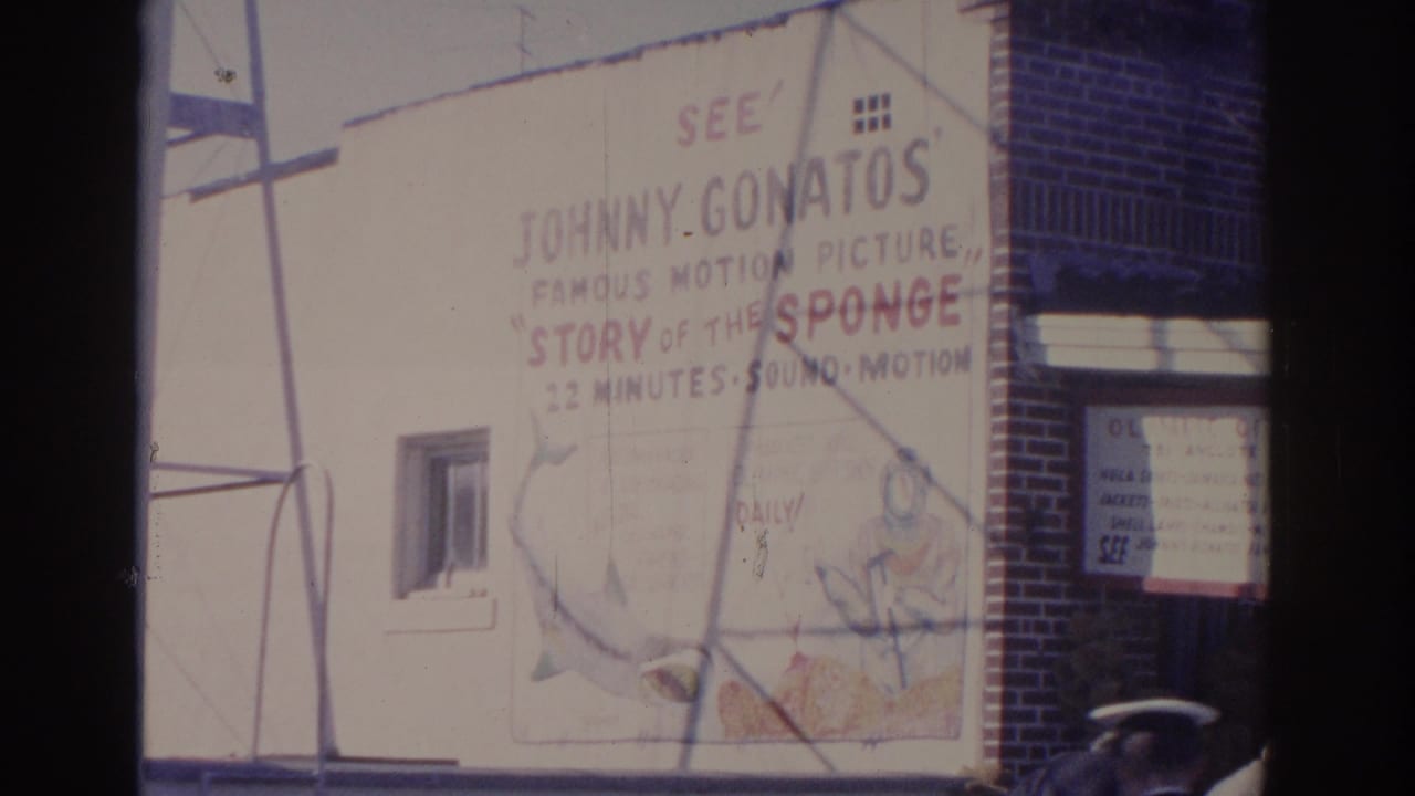 White building wall with painted movie advertisement and part of a brick entrance.