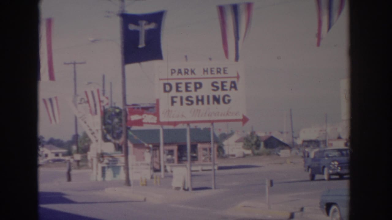 Deep sea fishing sign with flags and a blue pickup truck on the street.