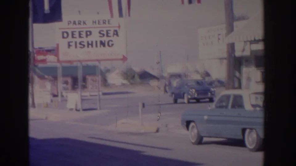 1962 Florida street footage with the deep sea fishing sign, passing 1960s cars, storefront edges, and bright roadside decorations.