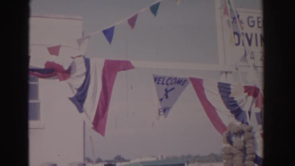 1962 Florida roadside building detail with red-white-blue bunting, triangular pennants, a partial welcome sign, and a partial diving sign.