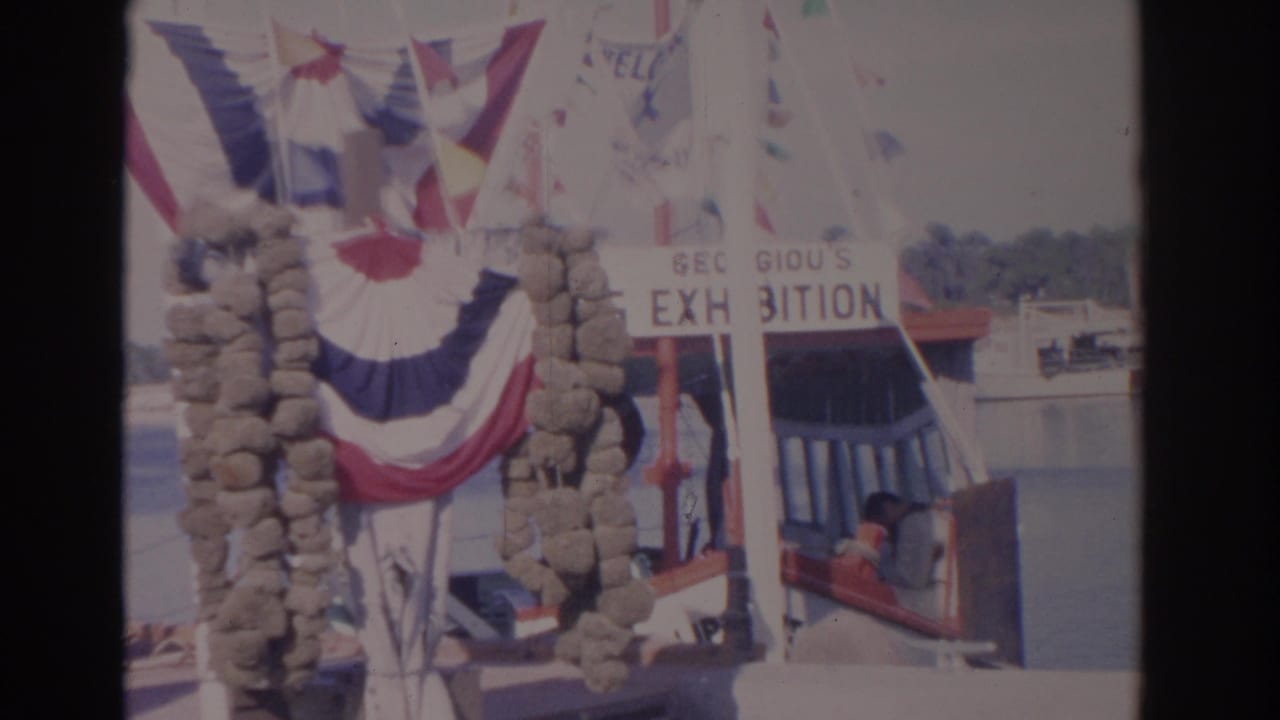 1962 Florida 8mm frame showing patriotic bunting beside a docked vessel at a harbor, with a partial exhibition sign visible.