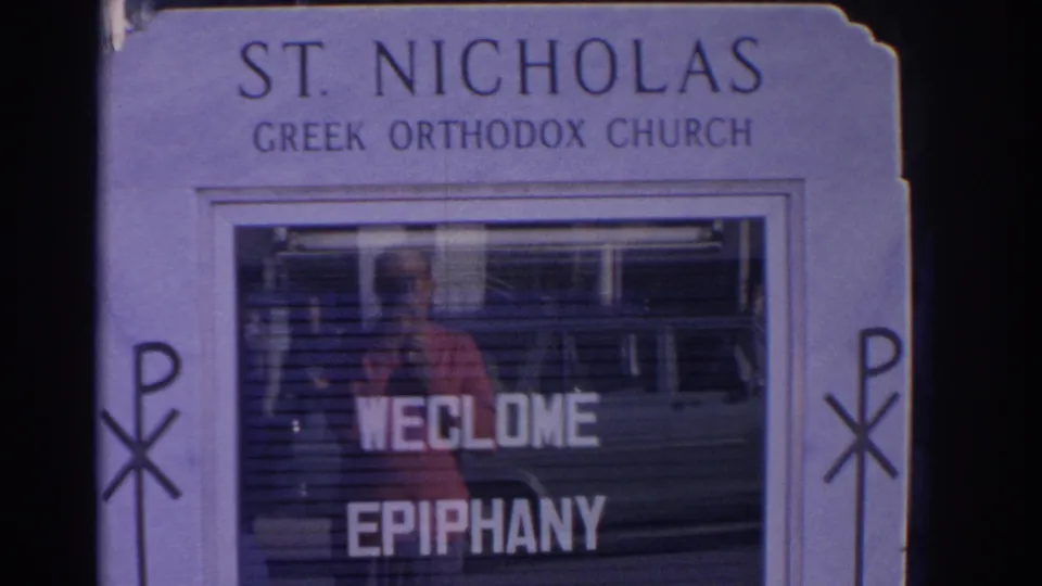 1962 Florida 8mm frame of a St. Nicholas Greek Orthodox Church sign with welcome epiphany lettering and street reflections in the glass.