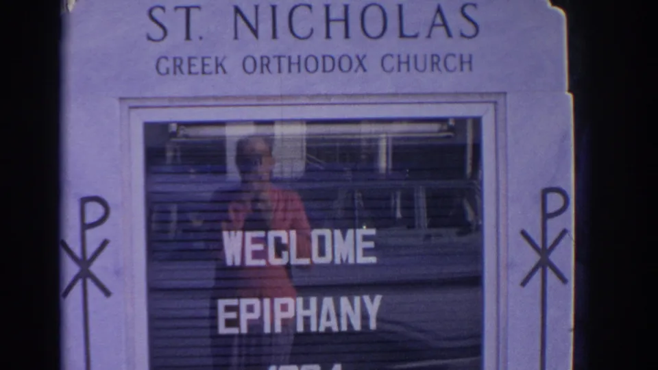 The St. Nicholas Greek Orthodox Church sign fills the frame, with welcome epiphany letters and reflected street detail in the glass.