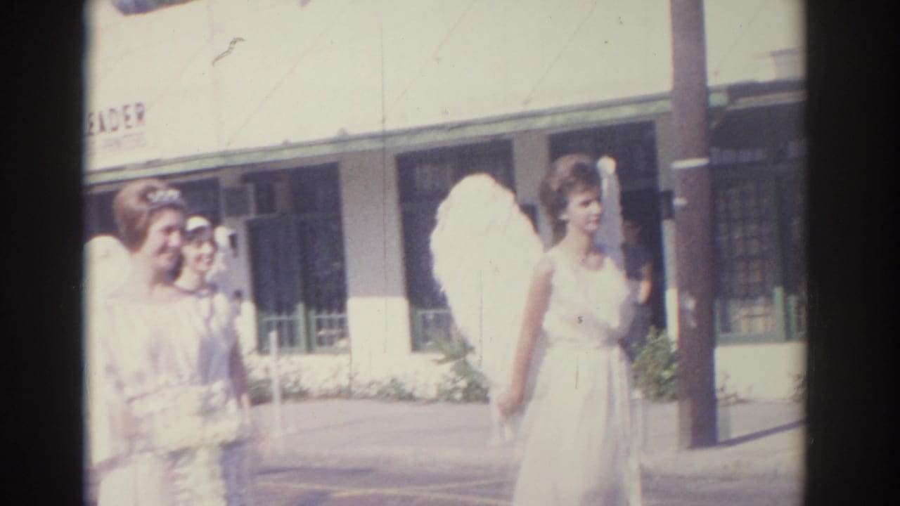 Women in white angel costumes stand on a sunny street near a storefront.