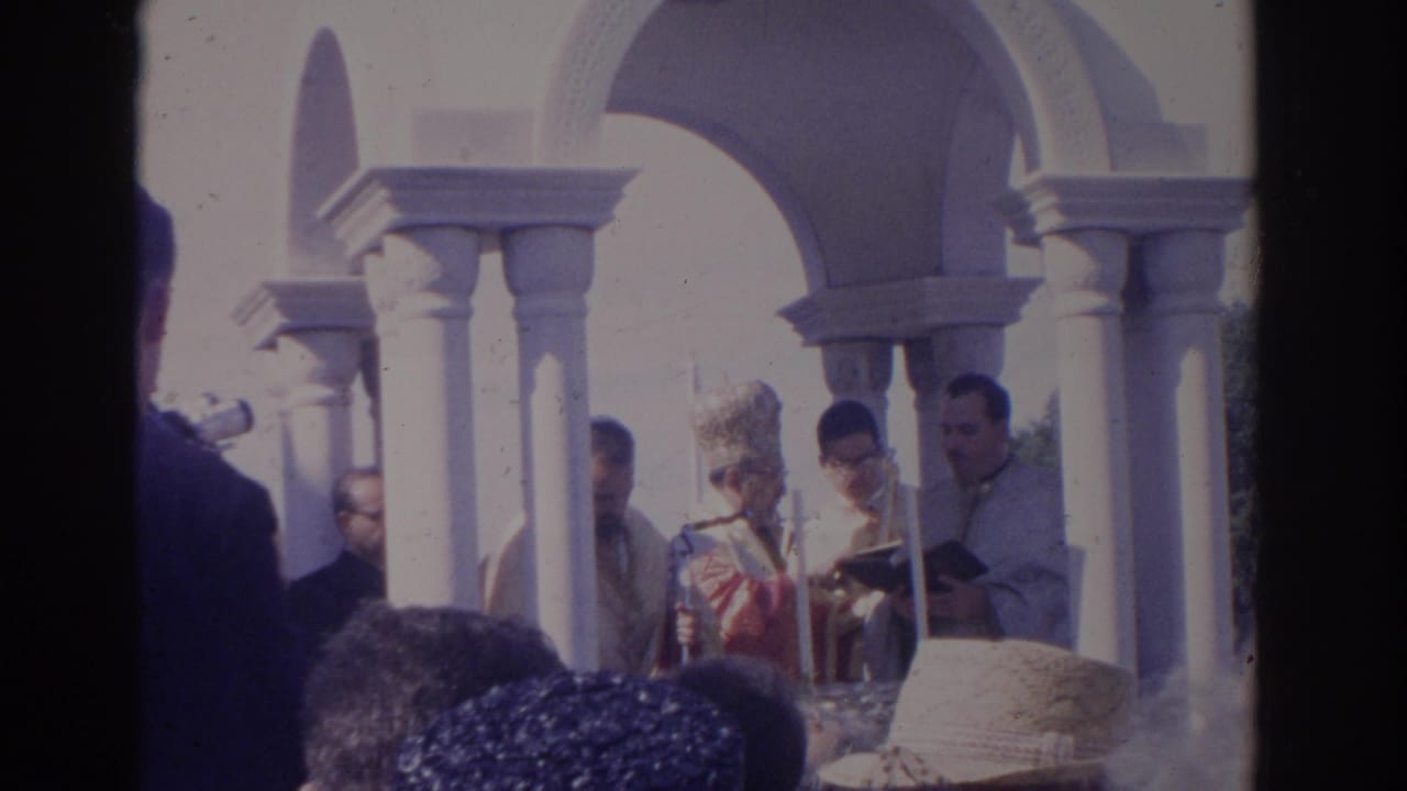 Bishop and clergy stand at an outdoor altar area beneath white columns.