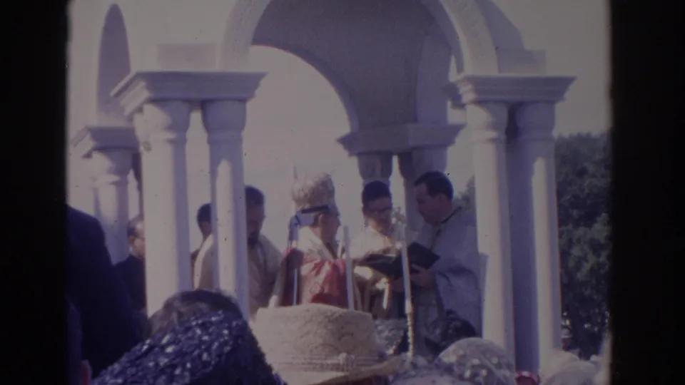 1962 Florida outdoor Catholic mass frame with clergy under white arches and the congregation partially visible in front.