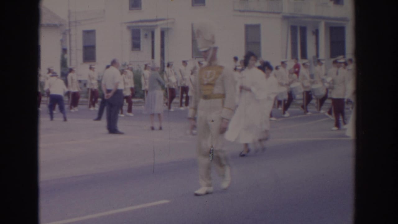 1962 Florida parade view with a cream-uniformed marcher, women in white dresses, and band members moving along a residential street.
