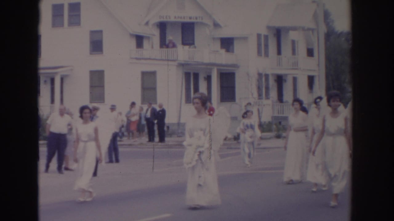 Women in white dresses and angel wings walk along a residential parade route.